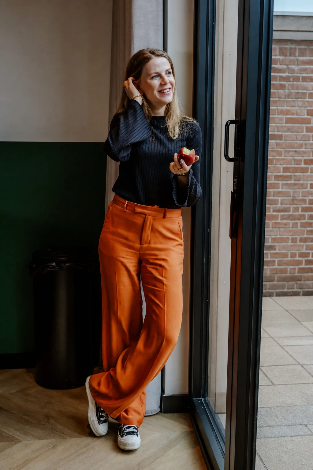 Fleur staat ontspannen bij het raam met een appel in haar hand